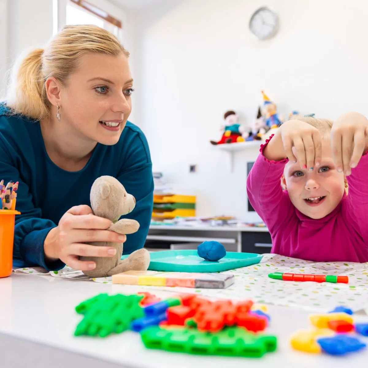 A therapist and a young child playing together at a table with clay and building toys
